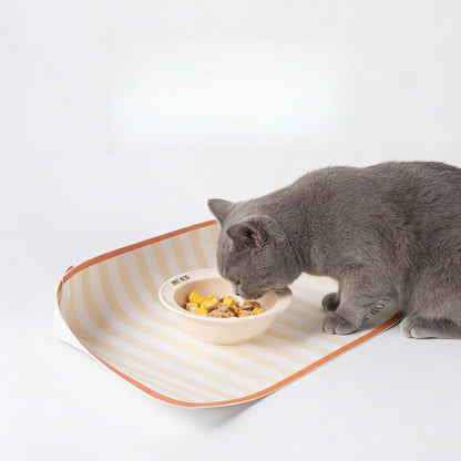 Cat eating from a bowl on a raised-edge striped feeding mat